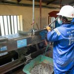 Trabalhador usando uma mesa vibratória para separar e processar minério em uma instalação industrial.