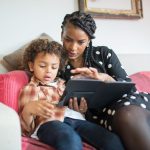 Mãe e filho usam juntos um tablet sentados em um sofá, em casa.