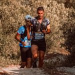 Dois corredores participam de uma prova de corrida em trilha por um caminho cercado de mata.